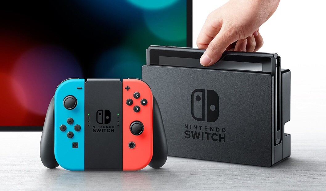 Nintendo Switch spillkonsoll med skjerm i ladestasjon, med to Joy-Con håndkontrollere satt i en Joy-Con Grip. Nintendo Switch spillkonsoll med skjerm i ladestasjon, med to Joy-Con håndkontrollere satt i en Joy-Con Grip.