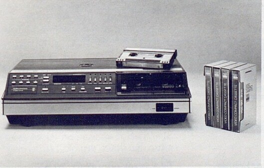 Et eksempel på det nye, europeiske Video 2000 systemet; her representert ved en maskin av Grundig-fabrikat. Grundig benytter U-båndføring i motsetning til Philips' M-båndføring, men en Philips-kassett kan likevel spilles på en Grundig-maskin og omvendt. Bilde fra Radiobransjen nr. 10/1979. Et eksempel på det nye, europeiske Video 2000 systemet; her representert ved en maskin av Grundig-fabrikat. Grundig benytter U-båndføring i motsetning til Philips' M-båndføring, men en Philips-kassett kan likevel spilles på en Grundig-maskin og omvendt. Bilde fra Radiobransjen nr. 10/1979.